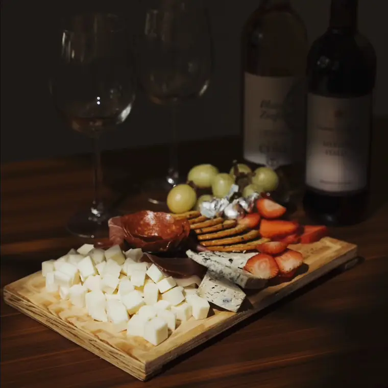 Tabla de quesos y carnes frías con uvas y fresas, junto a dos botellas de vino.