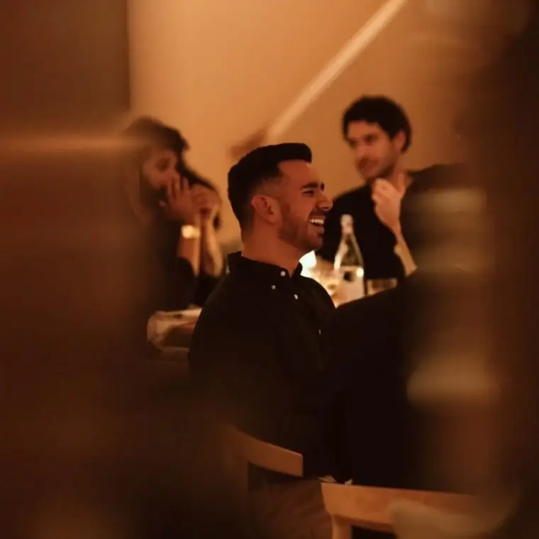 Invitados riendo en la mesa, iluminados por la luz cálida del comedor.