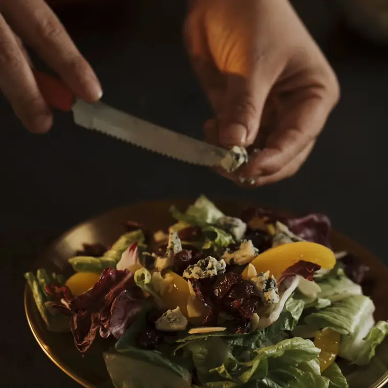 Ensalada con queso azul, arándanos y durazno servida en plato dorado.