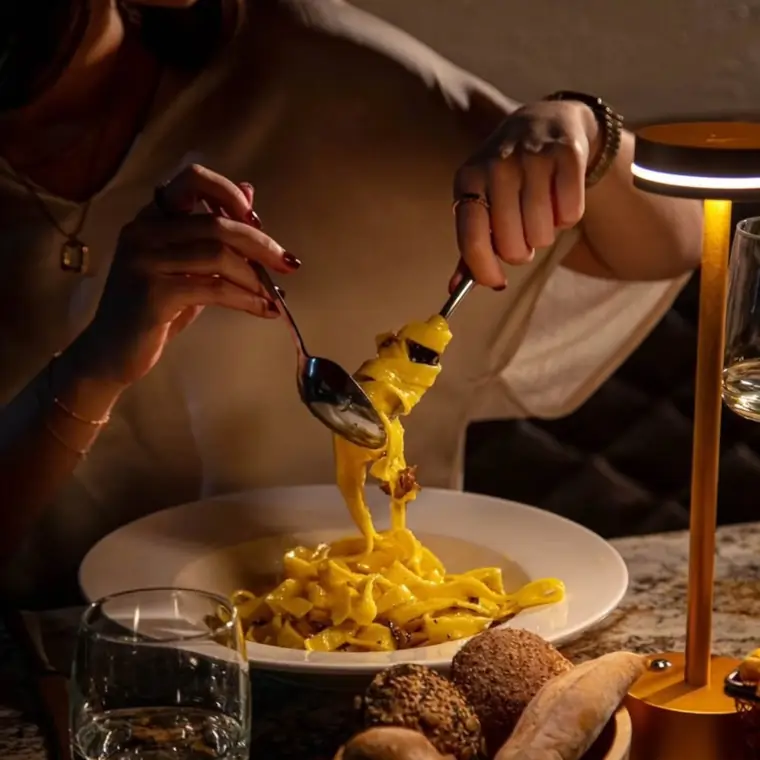 Fettuccine servido en la mesa, iluminado por una lámpara dorada.