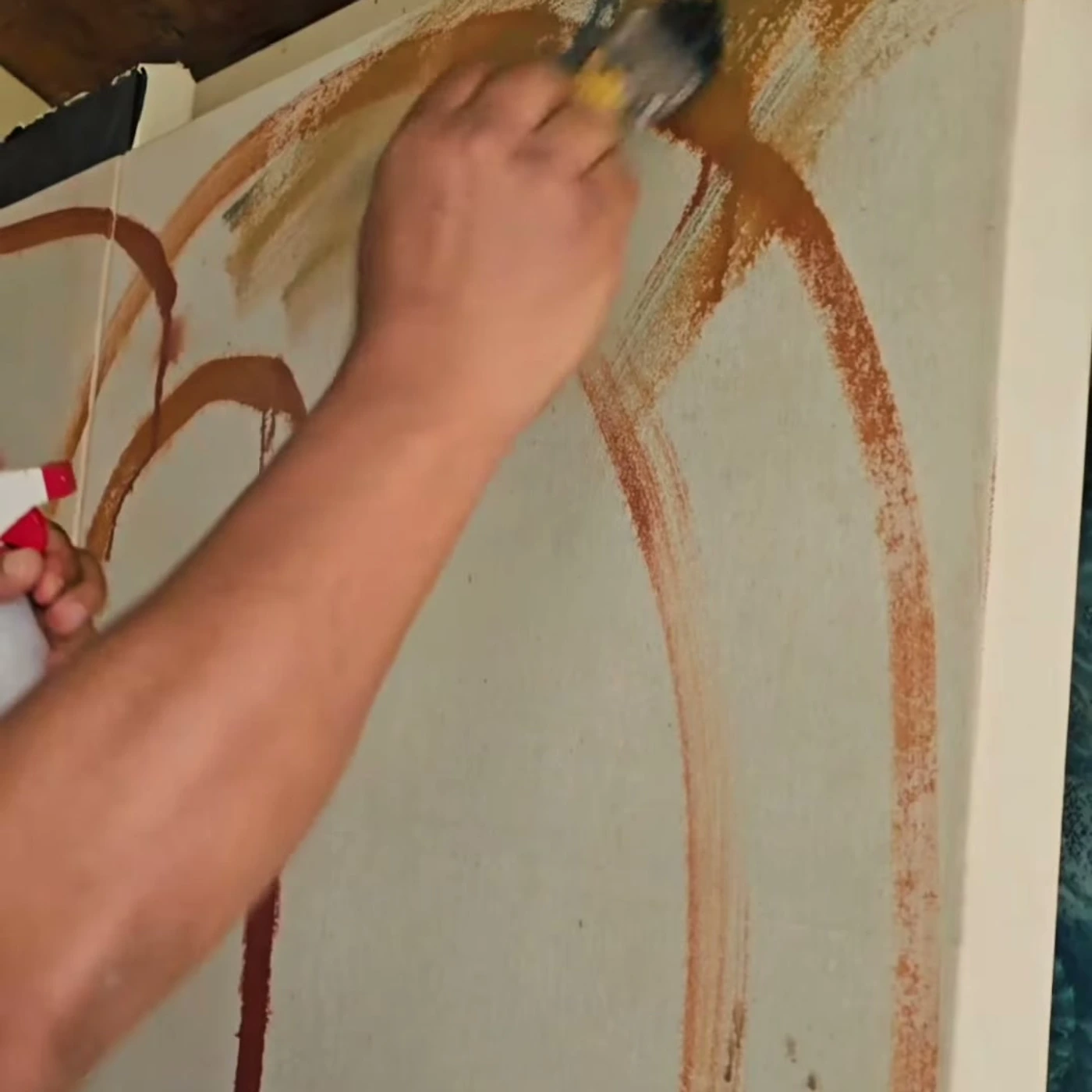 La mano del artista trazando en naranja y azul sobre el muro, durante la ejecución del mural.