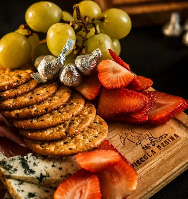 Detalle de la tabla: galletas de sésamo, uvas, fresas y queso azul sobre madera.