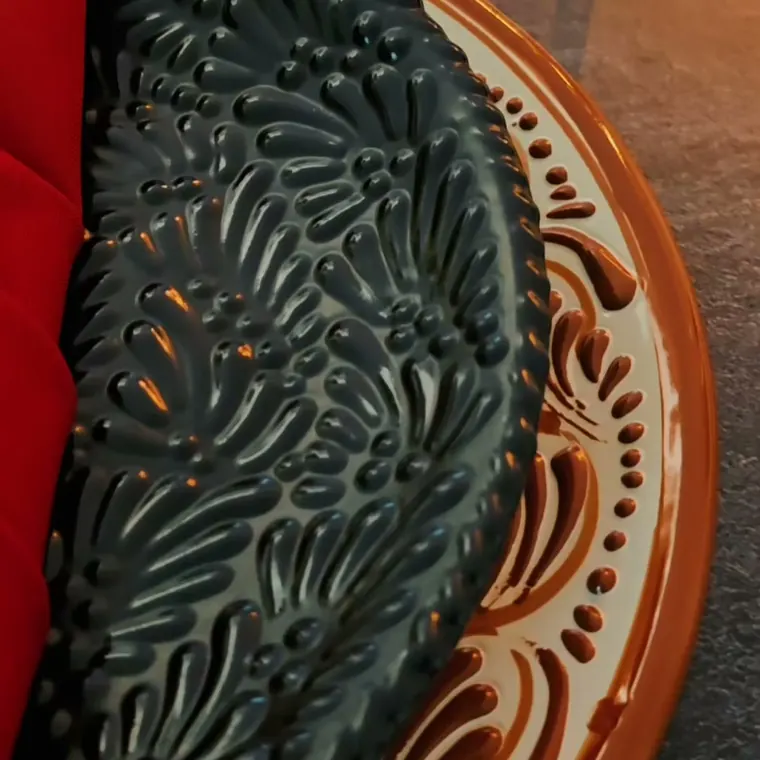 Plato de talavera negro en relieve con borde terracota y servilleta roja doblada.